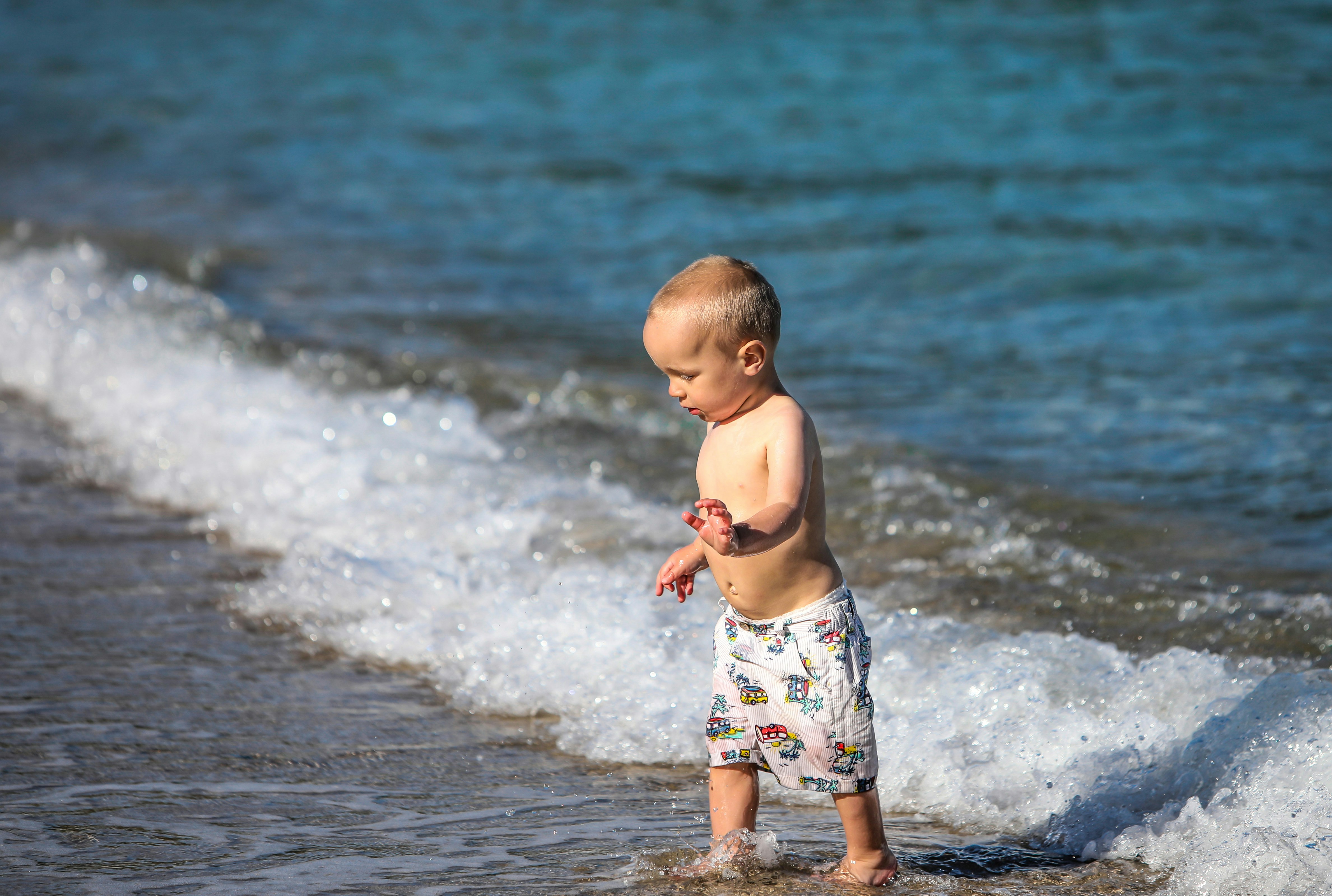 child in white and blue floral shorts standing on beach during daytime